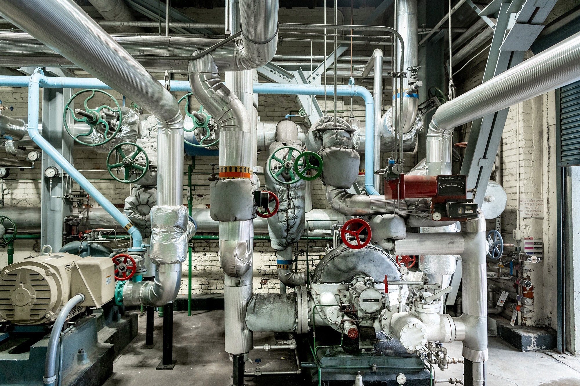 A tangled structure of pipes, valves, and other machinery covers the wall of a mechanical engineering job site.